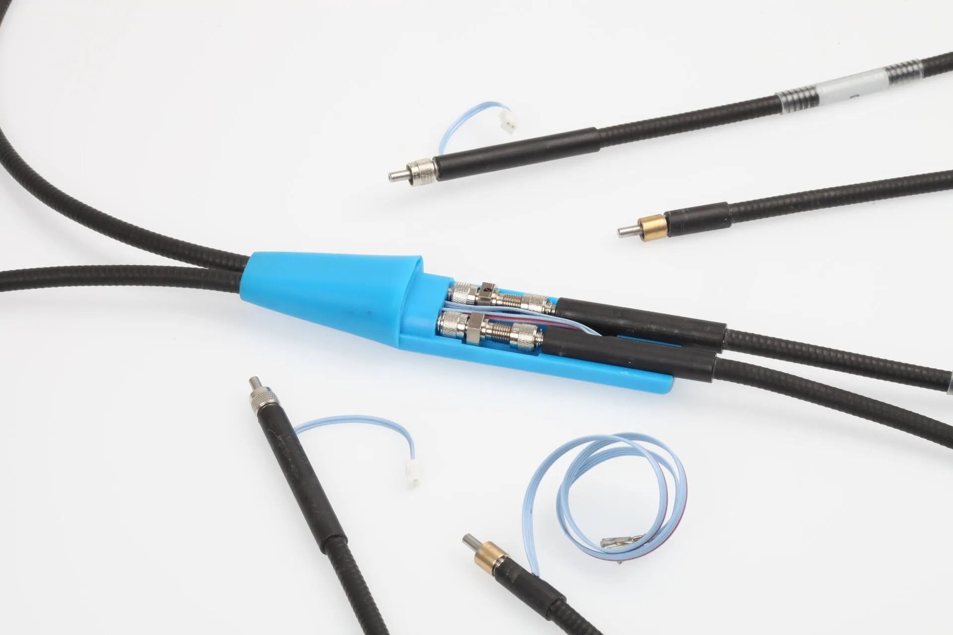 A detailed product shot showing a black cable splitting into two within a light blue plastic housing. Several other specialized terminated cables and a coiled wire are also visible on a white background.