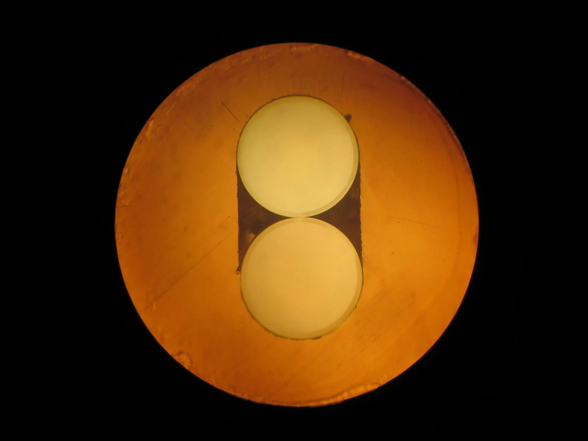A microscopic, circular view of the end of a fibre optic connector, showing two circular fibre cores against an orange background.