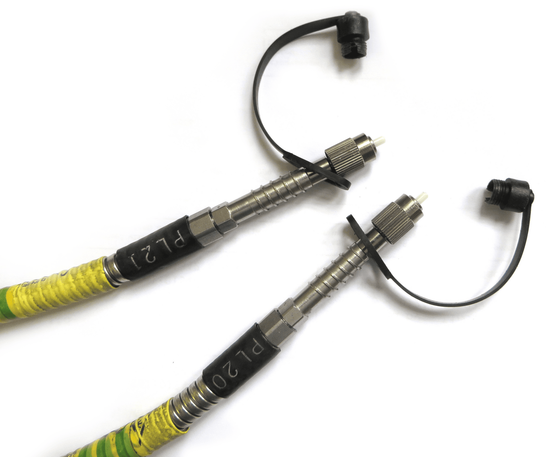 A detailed shot of two identical ruggedized fibre optic cable ends. Each cable has a yellow and black product label, a metal connector, and a black protective cap attached by a strap.