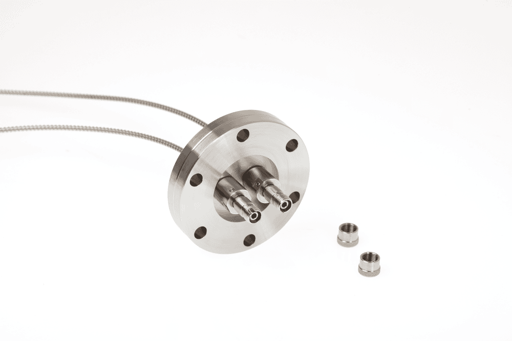 A detailed product shot of a circular metal flange with two central feedthroughs. Two ruggedized cables are shown attached to the back, and two separate threaded nuts are in the foreground.