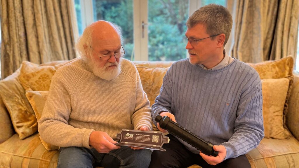 Alan and Richard Kershaw are pictured sitting on a sofa in a living room, holding an Alker Inline Splice Pipe.